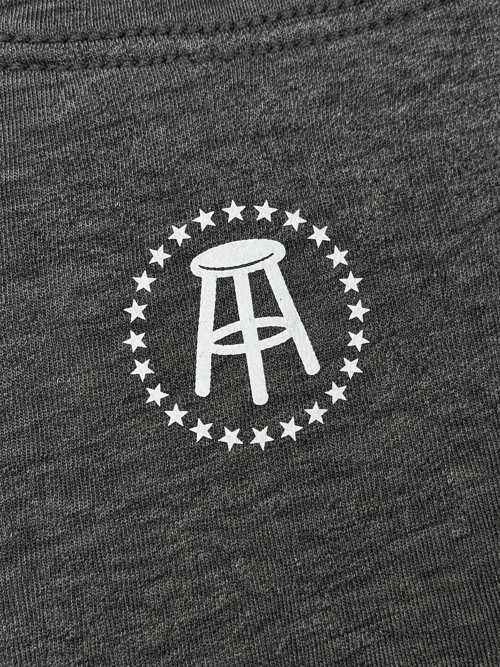 Close-up view of white stool logo and stars on upper back of heather-gray T-shirt