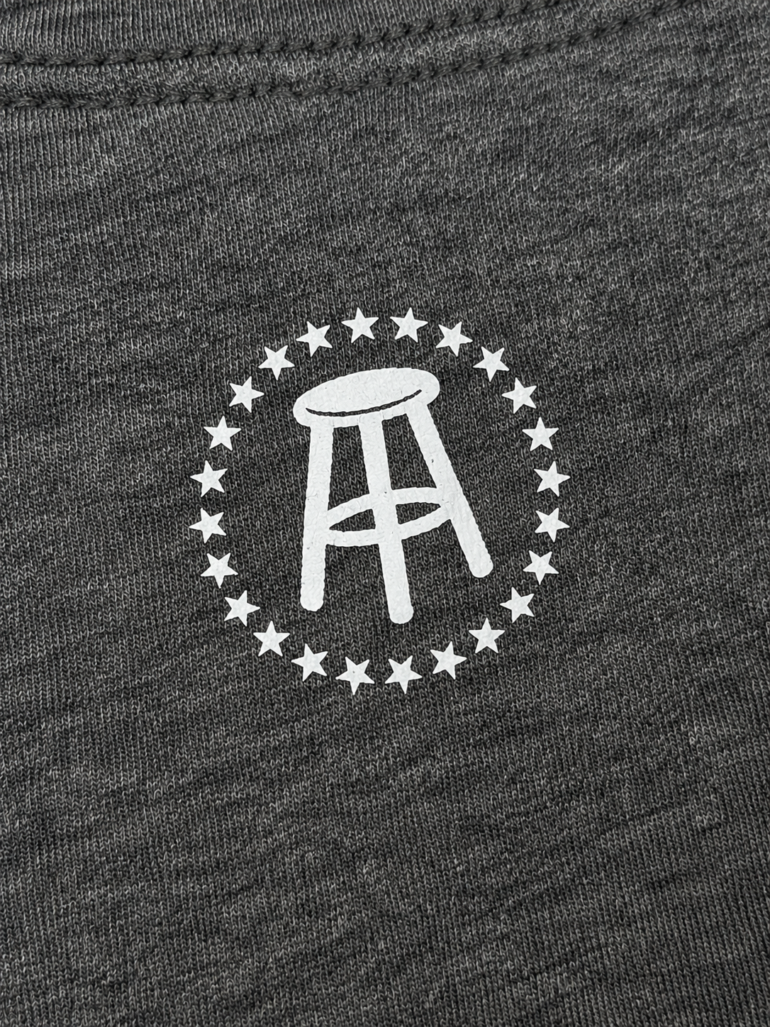 Close-up view of white stool logo and stars on upper back of heather-gray T-shirt