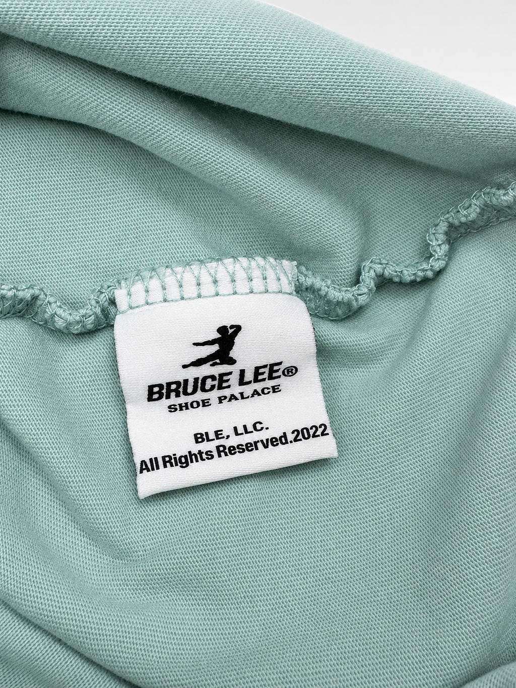 Close-up view of red Bruce Lee lettering and sleeve patch on mint T-shirt