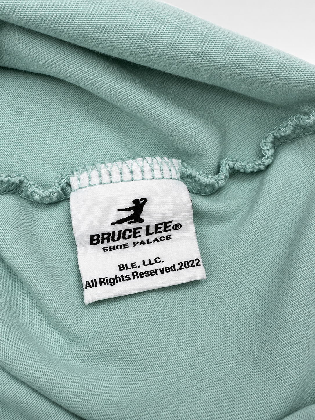 Close-up view of red Bruce Lee lettering and sleeve patch on mint T-shirt