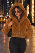 Styling image of a model wearing a copper hooded faux fur zip-front jacket with black jeans on a city street at night.