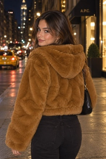 Rear styling view of a copper faux fur jacket, showing the hood down and banded hem, worn with black jeans at night.